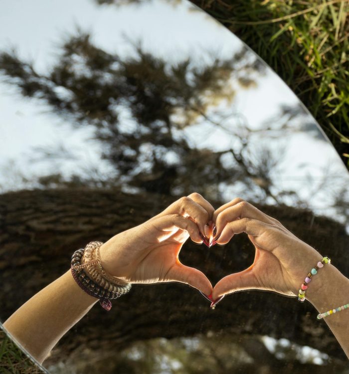 Reflection of hands forming a heart in a mirror outdoors, symbolizing love and connection.