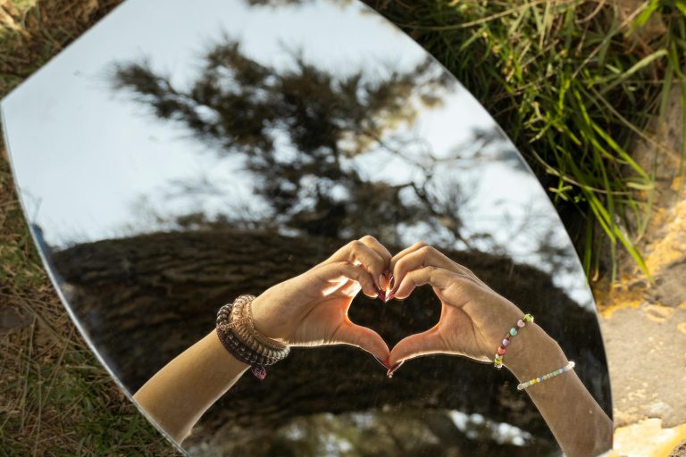 Reflection of hands forming a heart in a mirror outdoors, symbolizing love and connection.